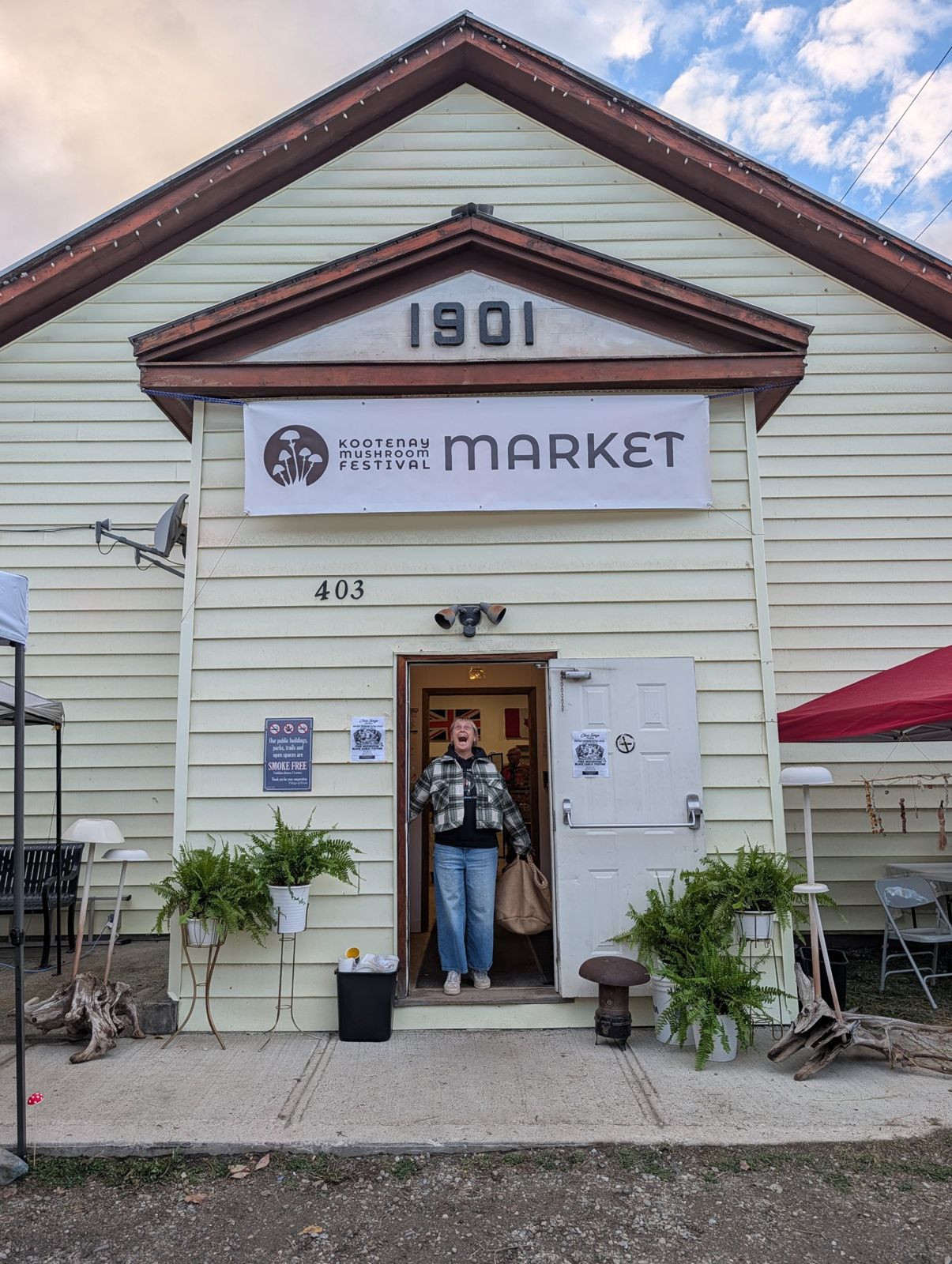 The 1901 Kaslo Legion hall with a Kootenay Mushroom Festival Market banner and a delighted visitor in the doorway